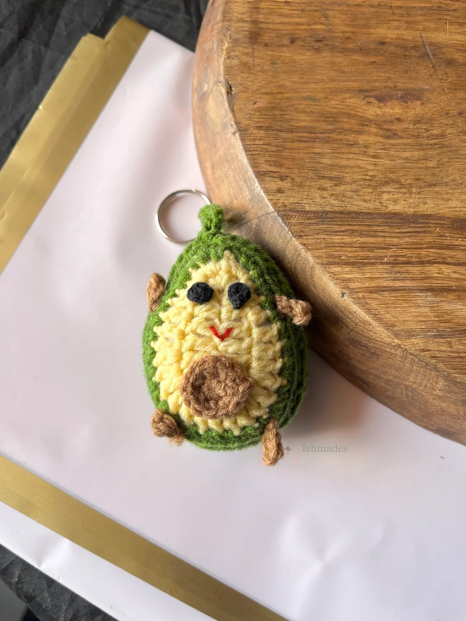 Handmade crochet avocado keychain with smiling face on wooden board