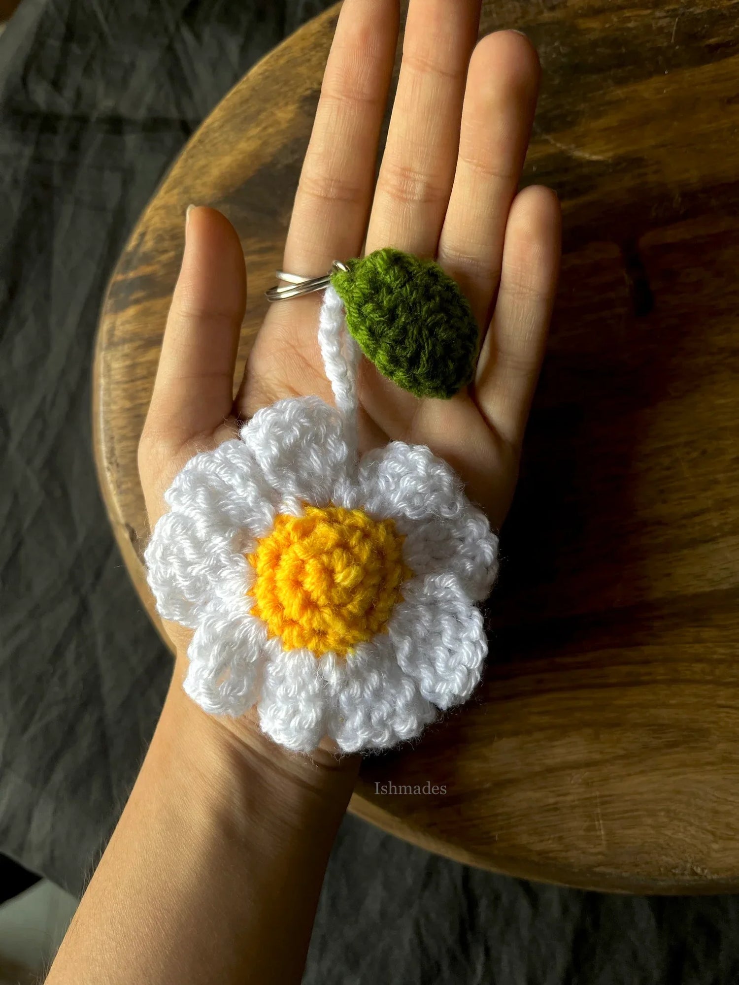 Hand holding a crocheted daisy keychain with white petals and a yellow center