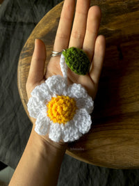 Hand holding a crocheted daisy keychain with white petals and a yellow center