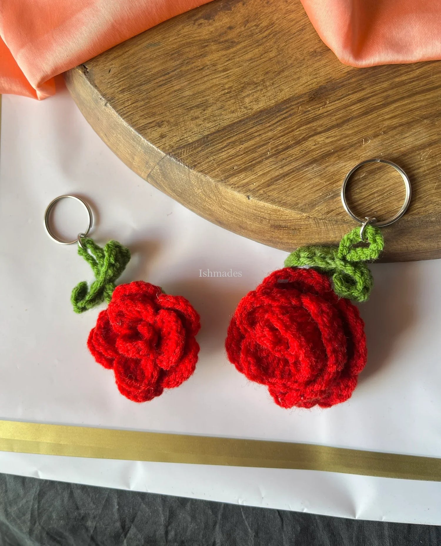 Handmade crochet red rose keychains with green leaves on a wooden tray