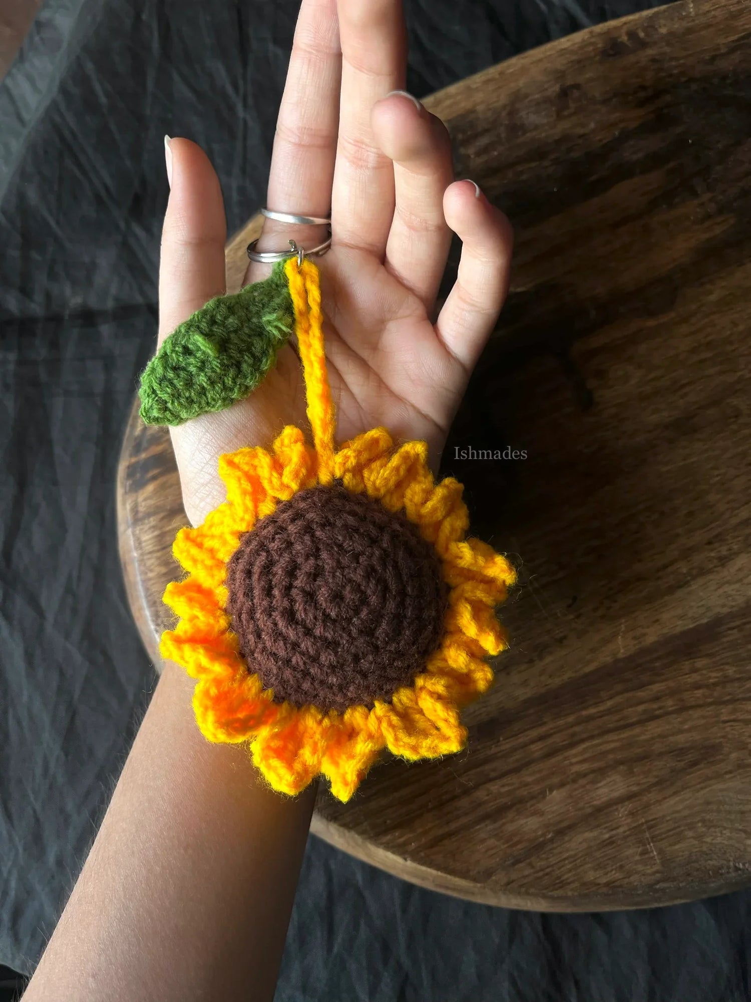 Hand holding a crocheted sunflower keychain with yellow petals and green leaf detail