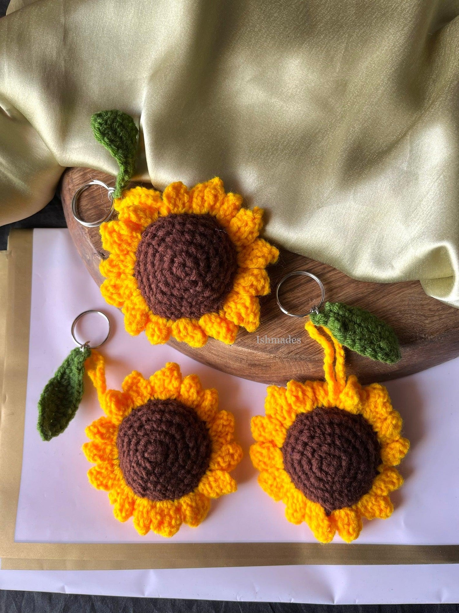 Handmade crochet sunflower keychains with yellow petals and green leaf detail on fabric