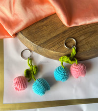 Handmade crochet flower keychains in pink and blue on wooden board, soft fabric background