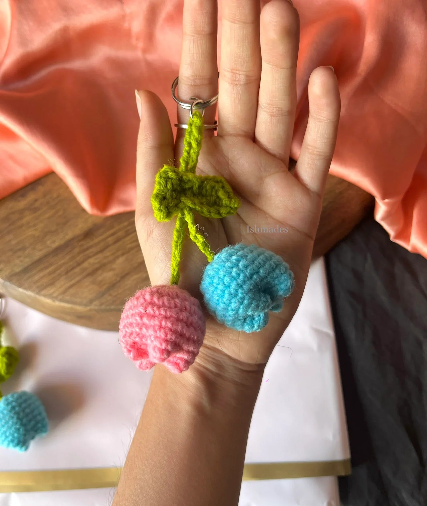 Hand holding crochet keychain with pink and blue flower-shaped charms and green leaves
