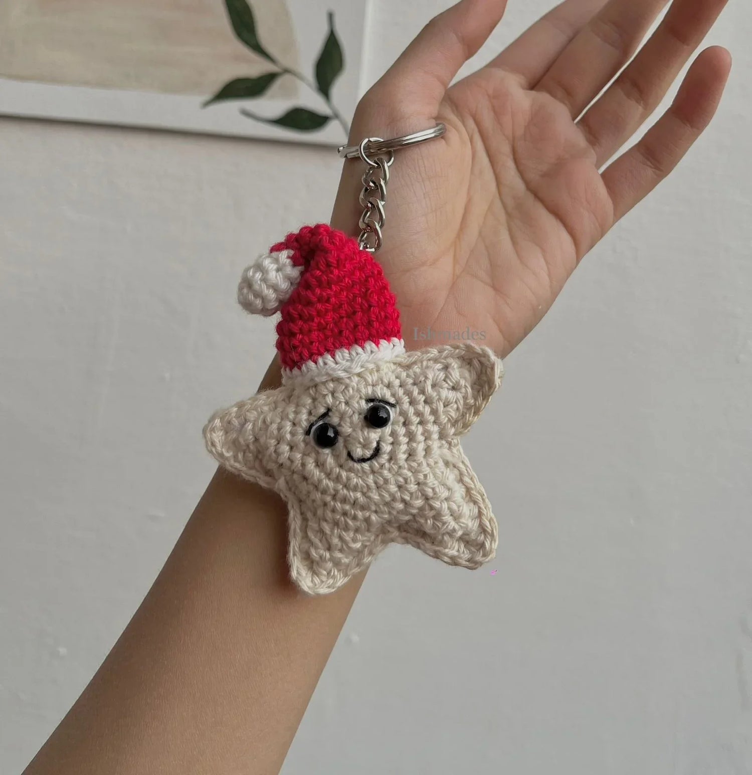 Hand holding crochet star keychain with Santa hat and smiling face