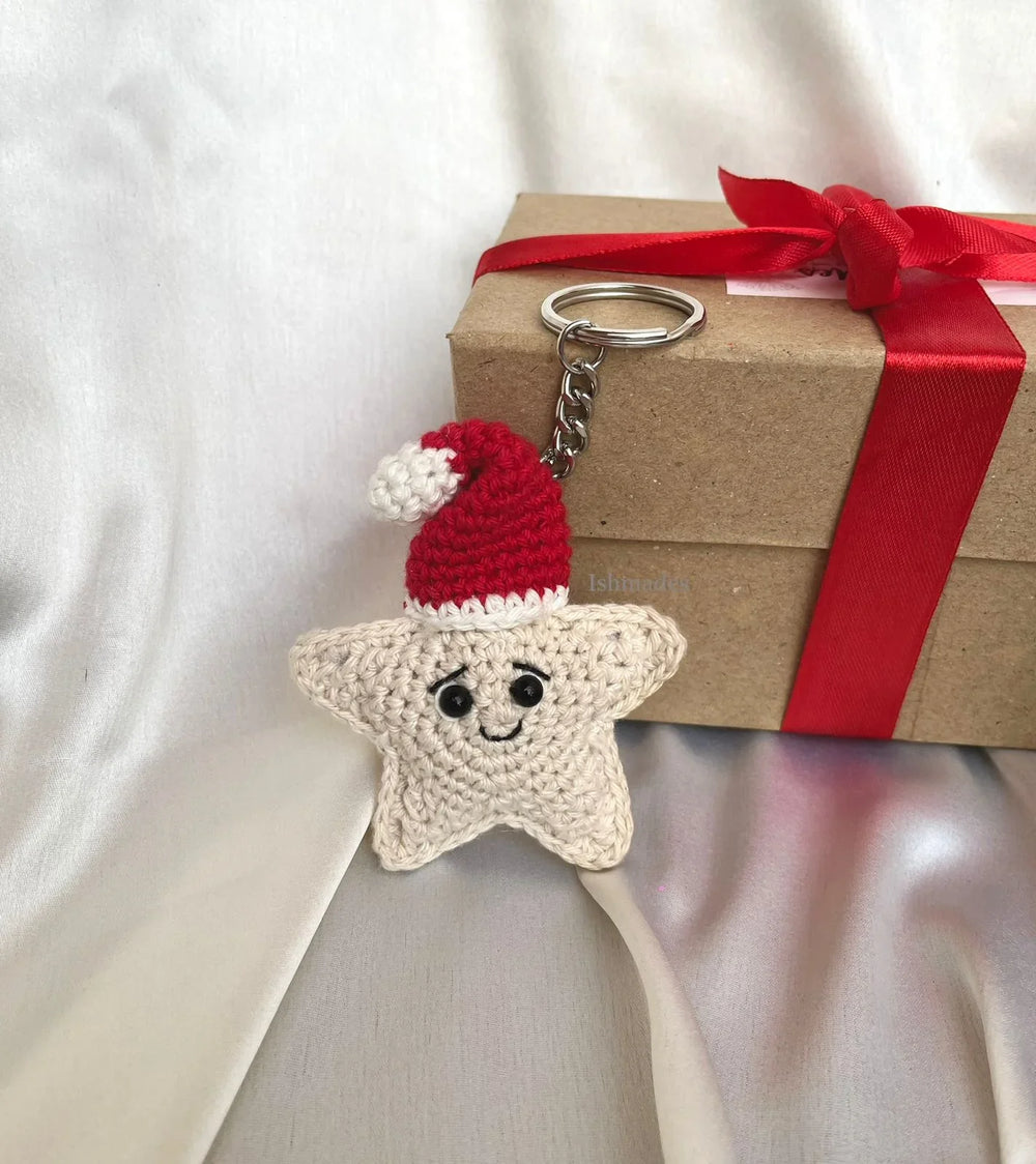 Crochet star keychain with Santa hat beside a gift box tied with a red ribbon