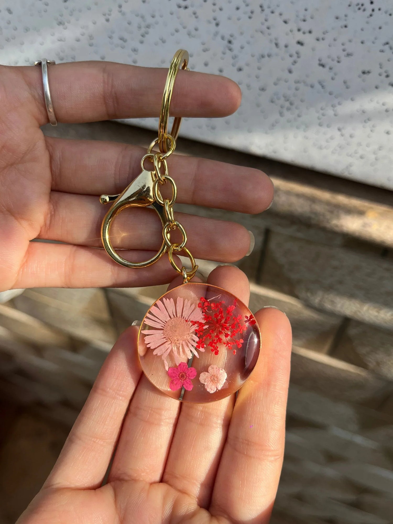 Gold keychain with pressed pink and red dried flowers in clear resin charm held in hand