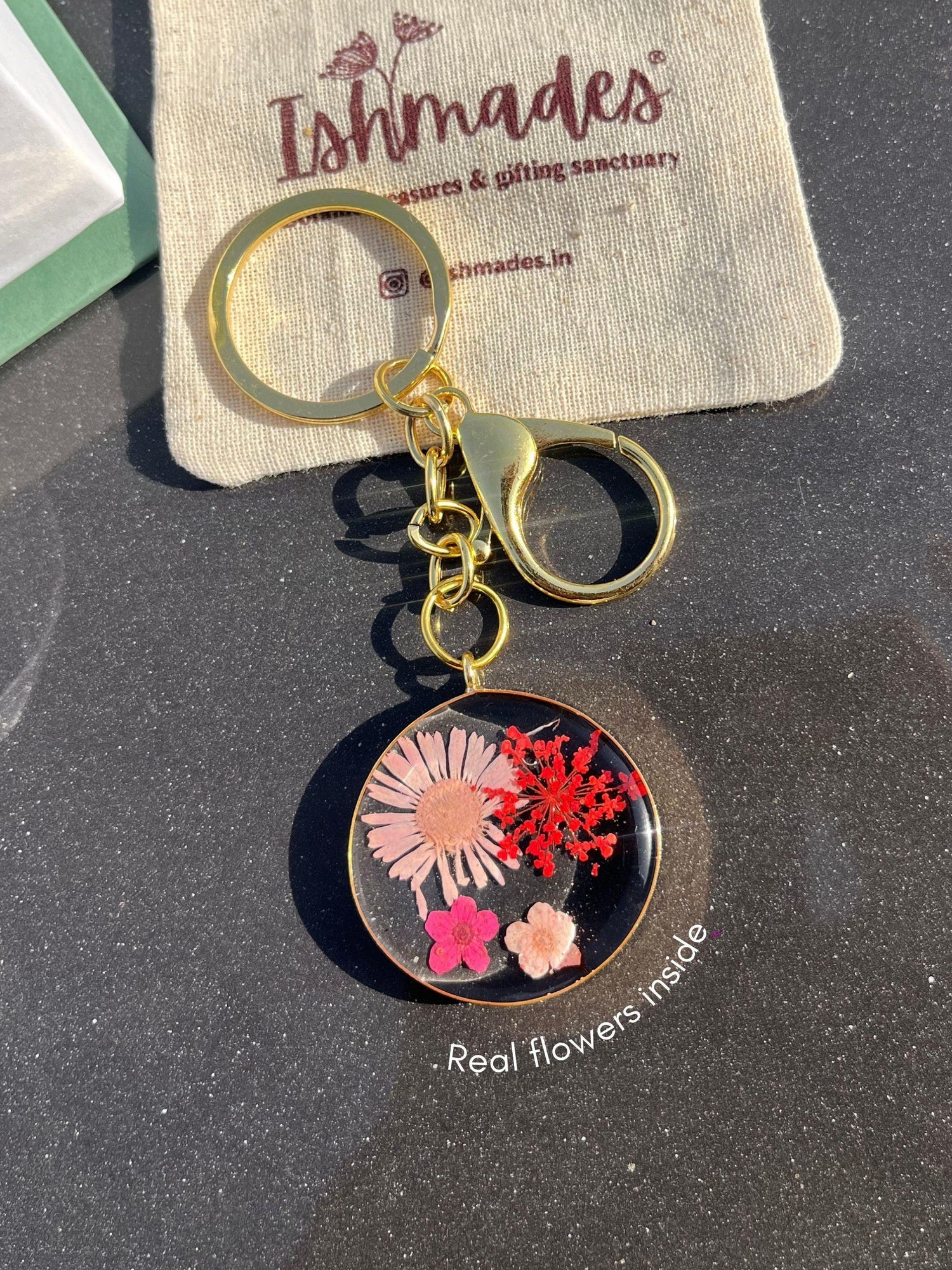 Gold keychain with pressed real flowers in clear resin, displayed on a black surface