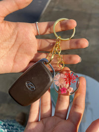 Hand holding a Hyundai car key with a gold keyring and floral resin keychain charm