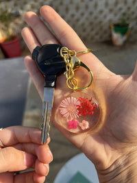Hand holding a car key with a round resin floral keychain featuring pink and red flowers