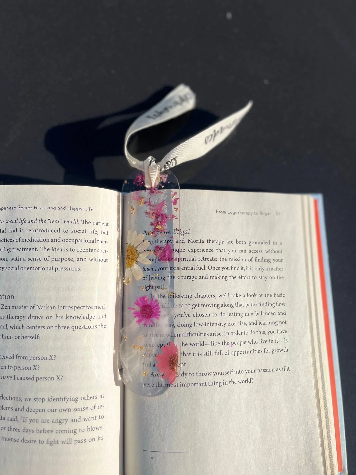 Pressed flower resin bookmark with ribbon on open book against black background