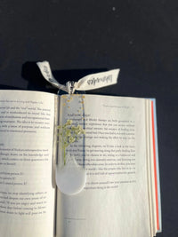 Pressed floral bookmark with ribbon on open book in sunlight
