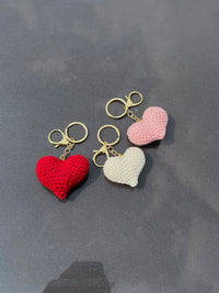 Three crochet heart keychains in red, white, and pink with gold rings on a gray surface.