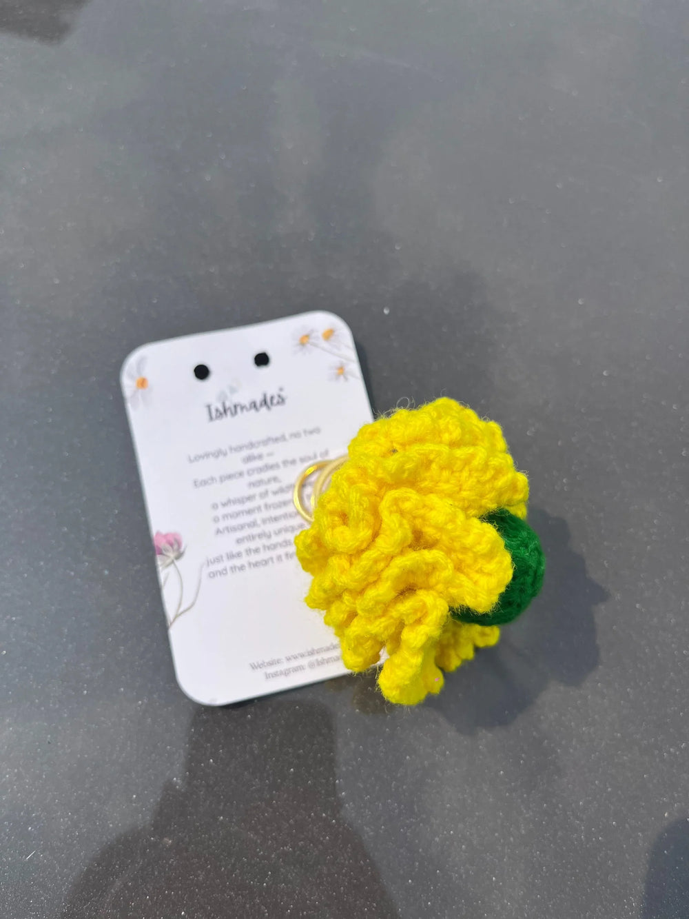Handmade yellow crochet flower keychain on a product card against a grey background