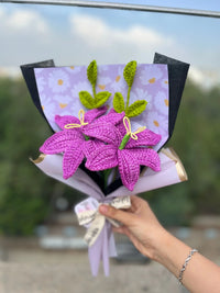 Hand holding a bouquet of purple crochet flowers with green leaves and decorative wrapping