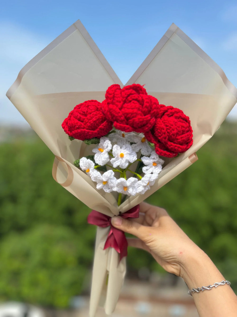 Hand holding bouquet of crocheted red roses and white flowers wrapped in beige paper