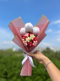 Hand holding a crochet flower bouquet wrapped in pink paper with a white ribbon outdoors