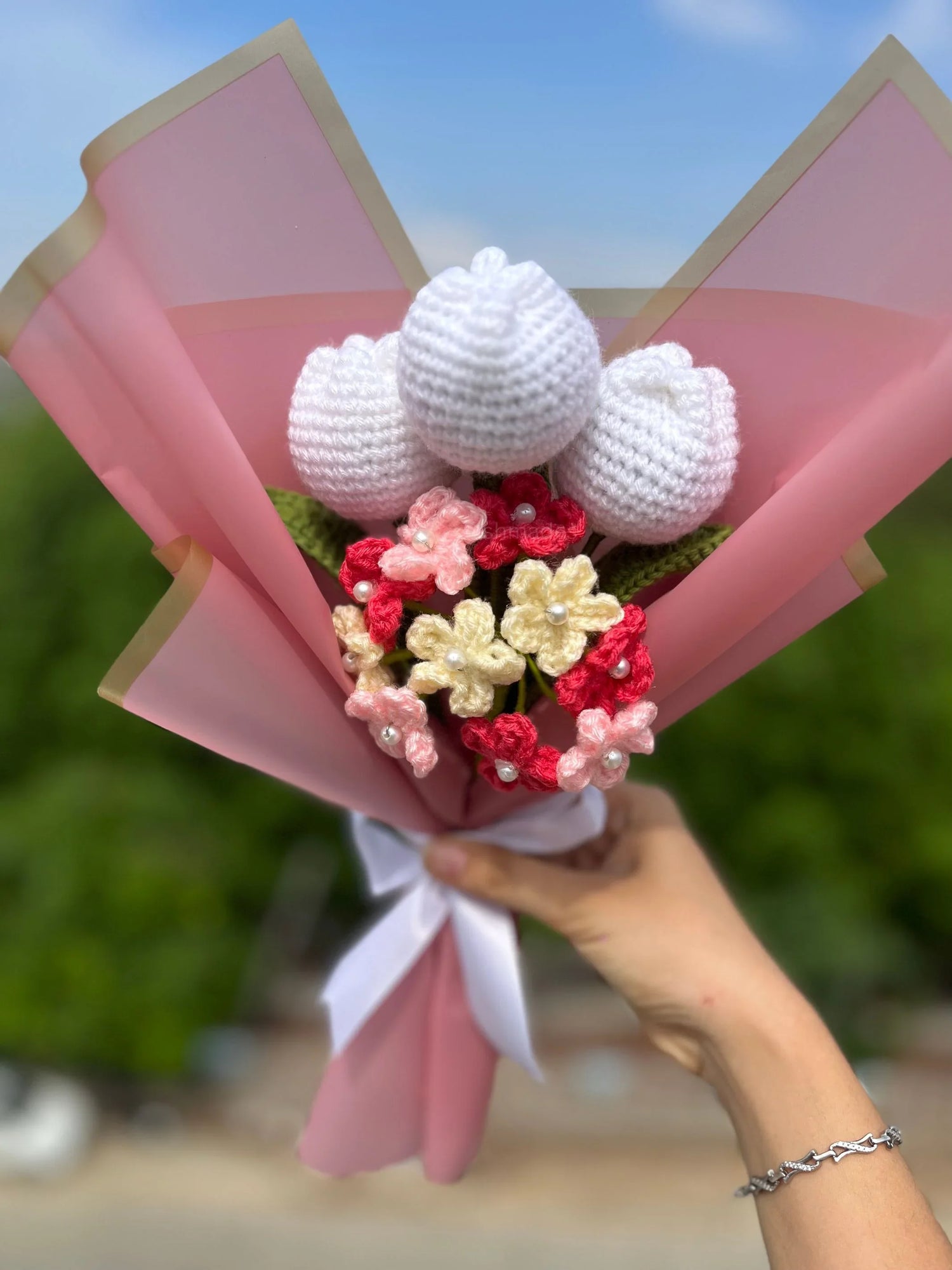 Hand holding crochet flower bouquet with white tulips and pink flowers, pink wrapping paper