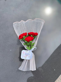 Bouquet of crocheted red roses wrapped in sheer white paper with a ribbon tag
