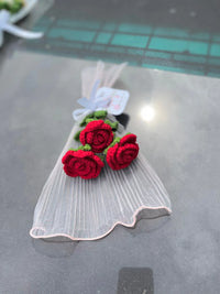 Handmade crochet red rose bouquet wrapped in sheer white fabric on a reflective surface