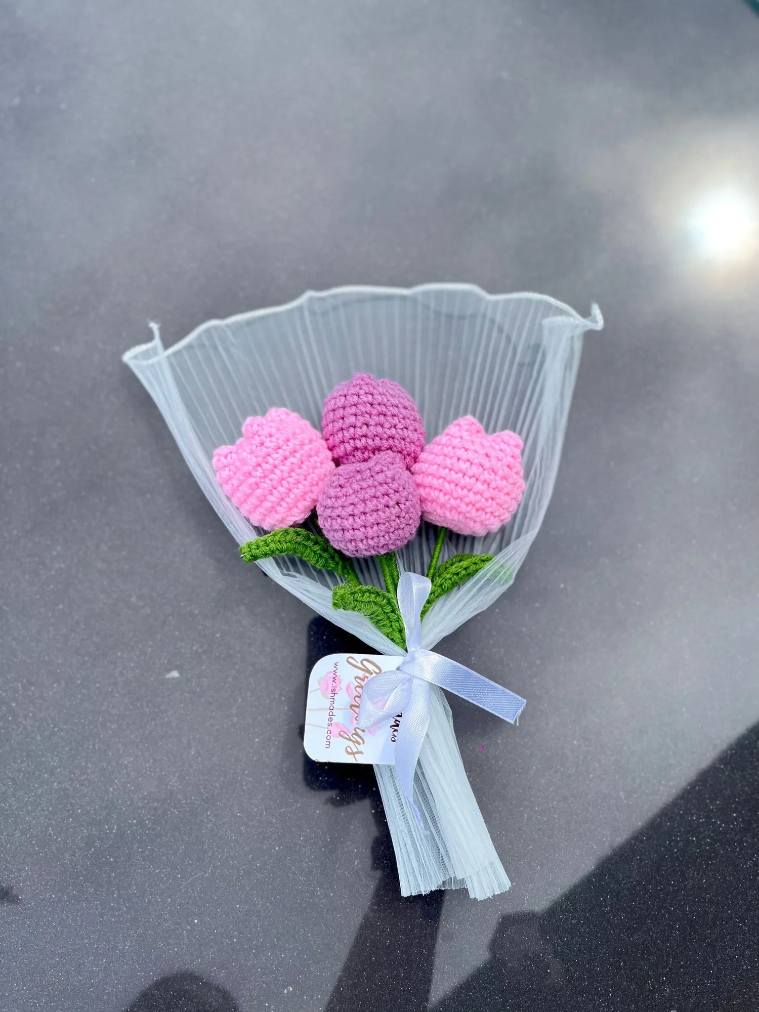 Handmade crochet tulip bouquet in pink and purple with white ribbon, displayed on gray surface