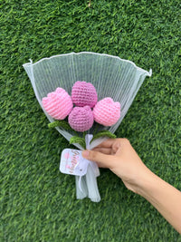 Hand holding a bouquet of pink and purple crochet tulips wrapped in white paper