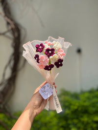 Hand holding a bouquet of pink, white, and burgundy crochet flowers with pearl centers