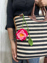 Woman holding black and white striped tote bag with crochet flower bag charm
