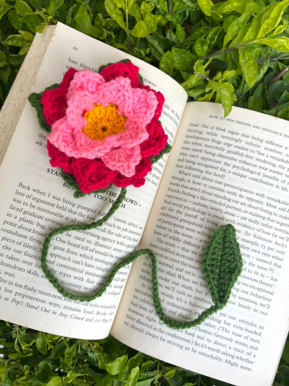 Handmade crochet flower bookmark on open book with green leaves in background