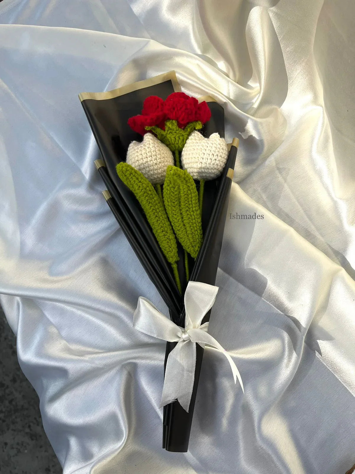Handmade crochet flower bouquet with white and red blooms wrapped in black paper on satin fabric