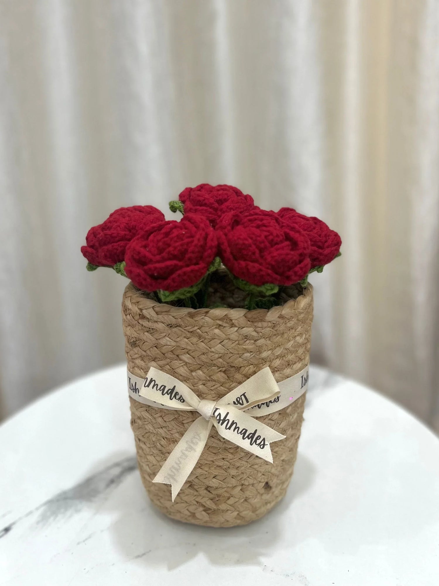Handmade red crochet roses in a woven basket with cream ribbon on a marble table