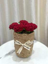 Handmade red crochet roses in a woven basket with cream ribbon on a marble table