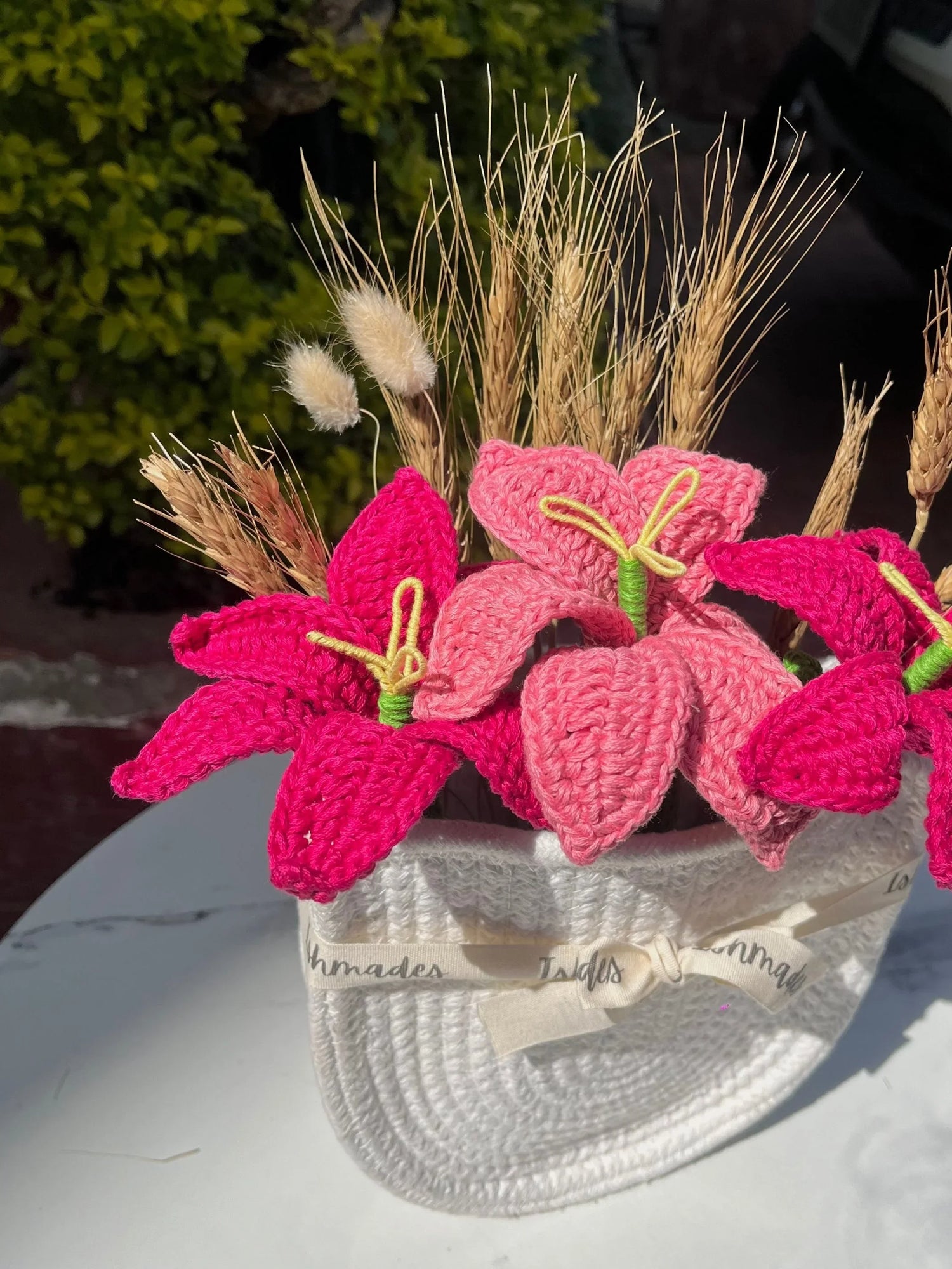Handmade crochet pink flowers and dried wheat stems arranged in a white woven basket