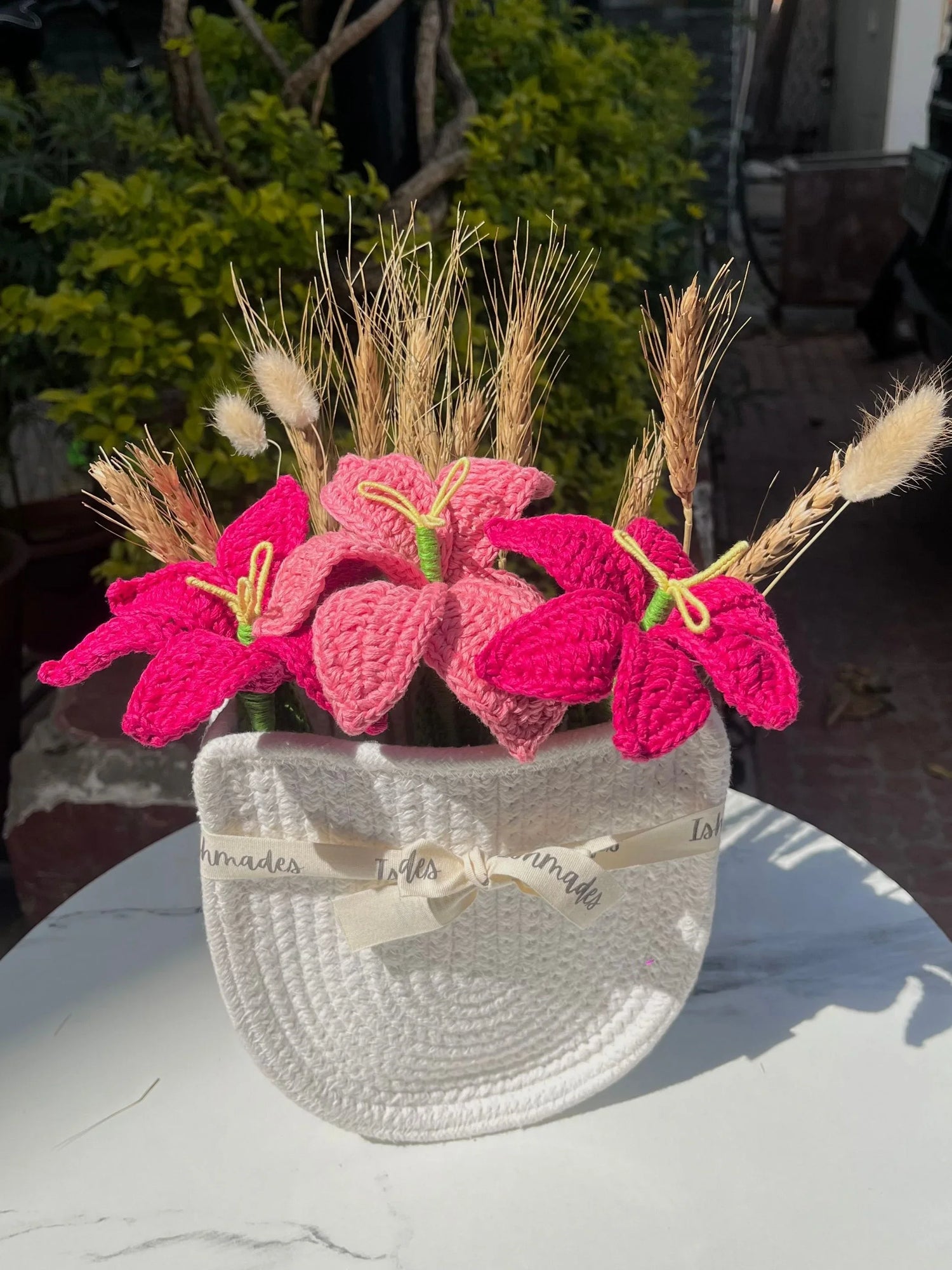 Pink crochet flowers and dried wheat in a white woven hat basket on a marble table