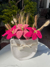 Pink crochet flowers and dried wheat in a white woven hat basket on a marble table