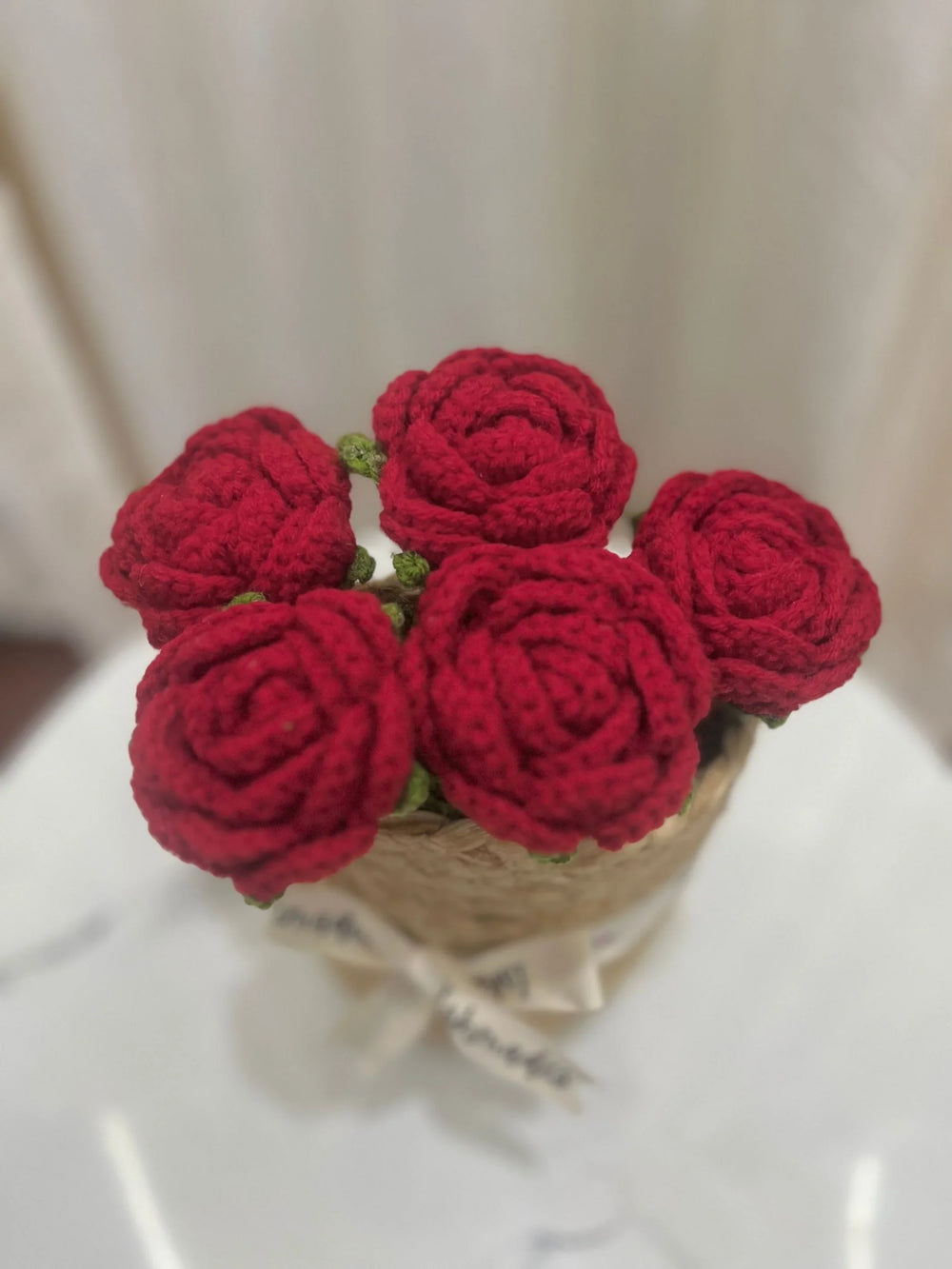 Handmade crochet red rose bouquet in a small basket with a ribbon, soft background