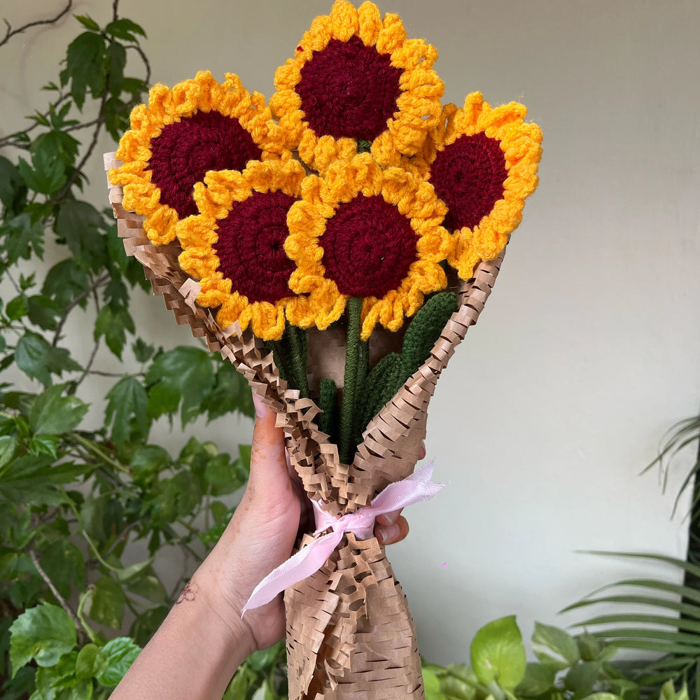 Hand holding bouquet of yellow and red crochet sunflowers wrapped in brown paper