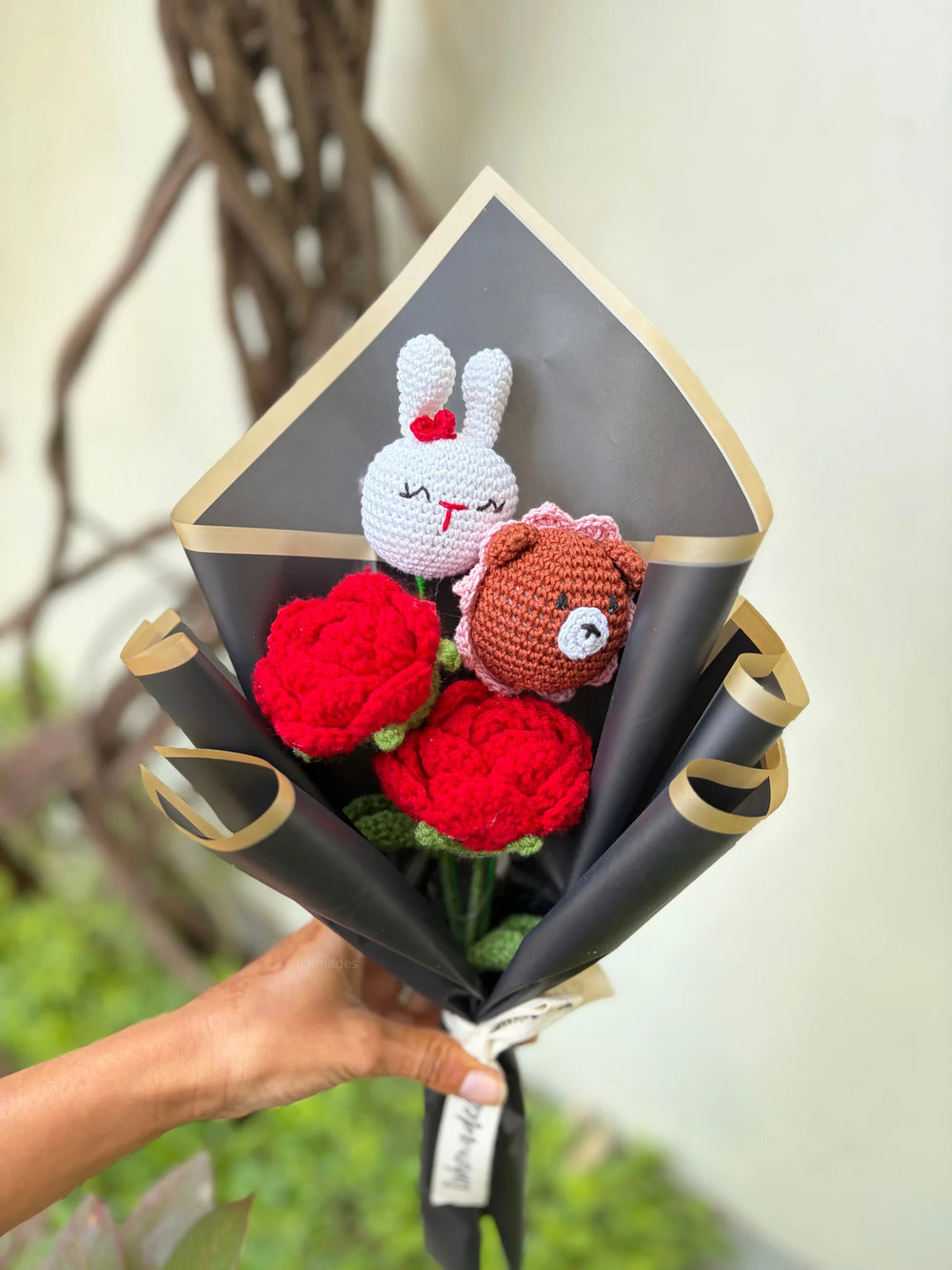 Hand holding a bouquet of crocheted red roses with cute bunny and bear plush toys.