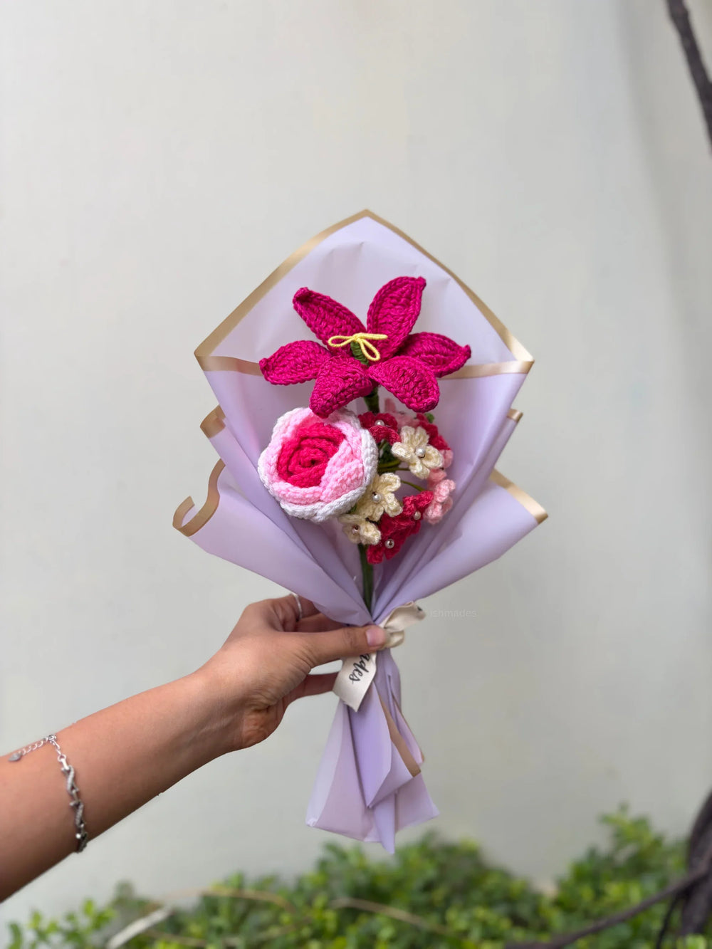 Hand holding a bouquet of pink crochet flowers wrapped in pastel paper