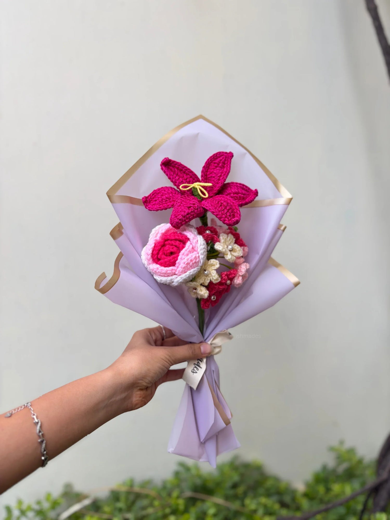 Hand holding a bouquet of pink crochet flowers wrapped in pastel paper