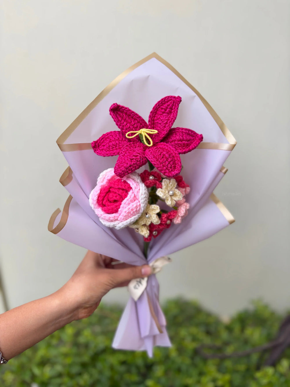 Hand holding a crochet flower bouquet with pink and white flowers wrapped in pastel paper