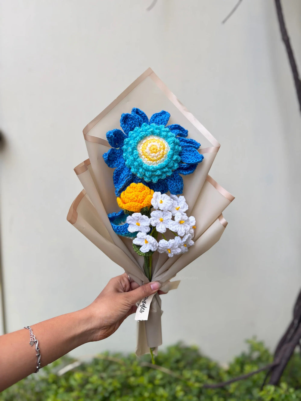 Hand holding a bouquet of colorful crochet flowers wrapped in beige paper