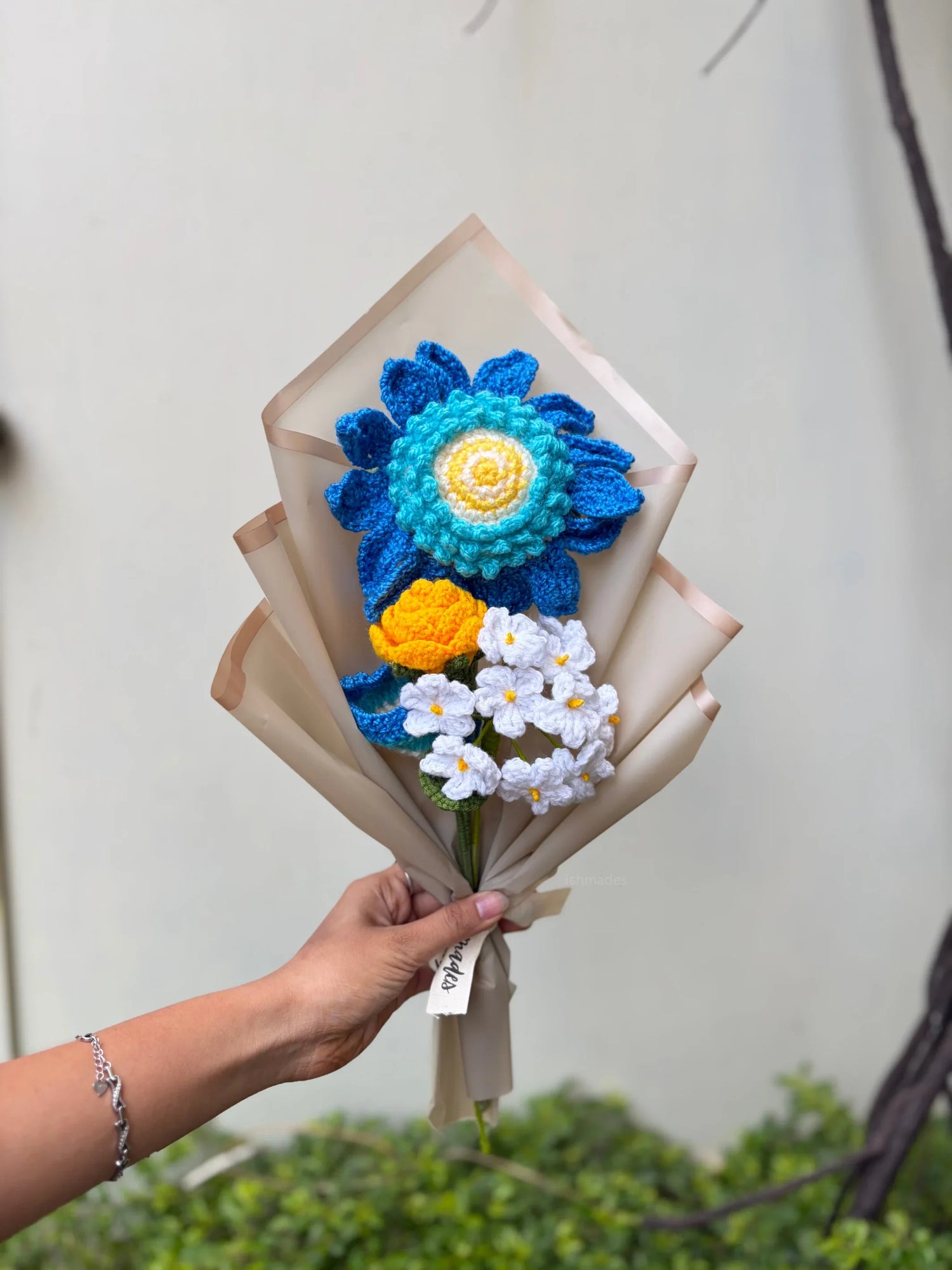 Hand holding a bouquet of colorful crochet flowers wrapped in beige paper