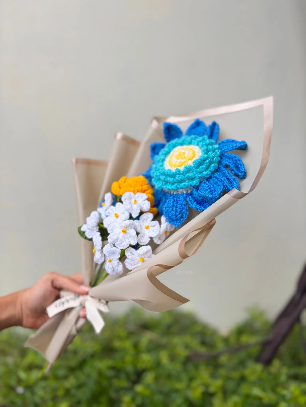Hand holding a bouquet of colorful crocheted flowers wrapped in beige paper