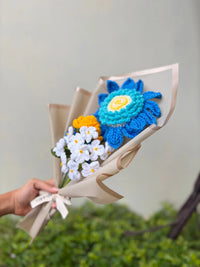 Hand holding a bouquet of colorful crocheted flowers wrapped in beige paper