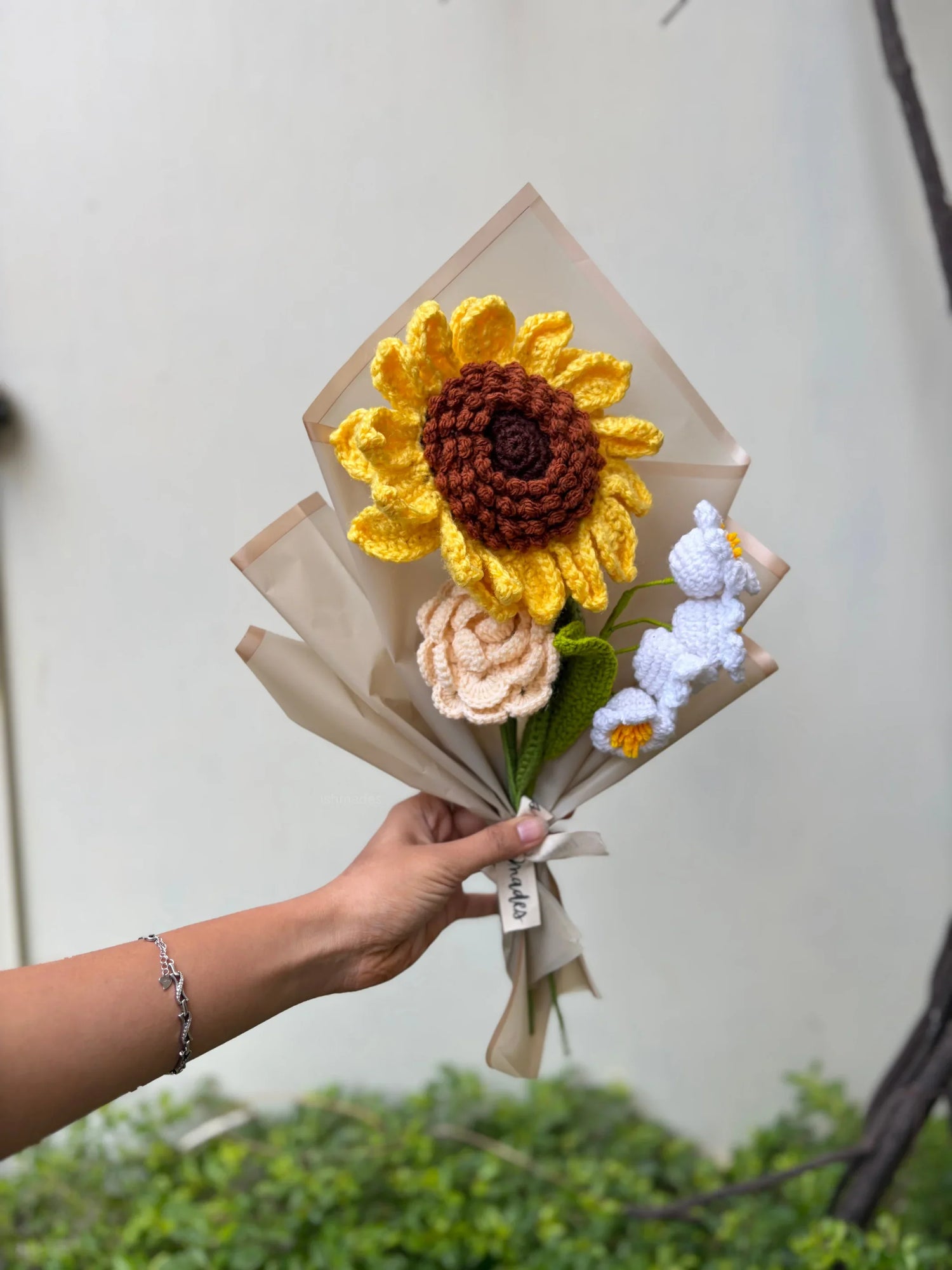 Hand holding a bouquet of crochet flowers with a sunflower centerpiece, gift wrapped.