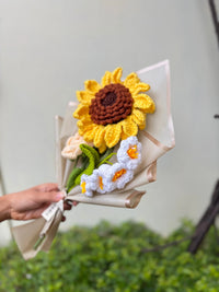 Hand holding bouquet of crocheted sunflower and white flowers wrapped in paper