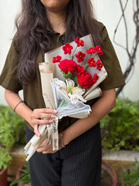 Woman holding a bouquet of red and white crochet flowers wrapped in paper outdoors