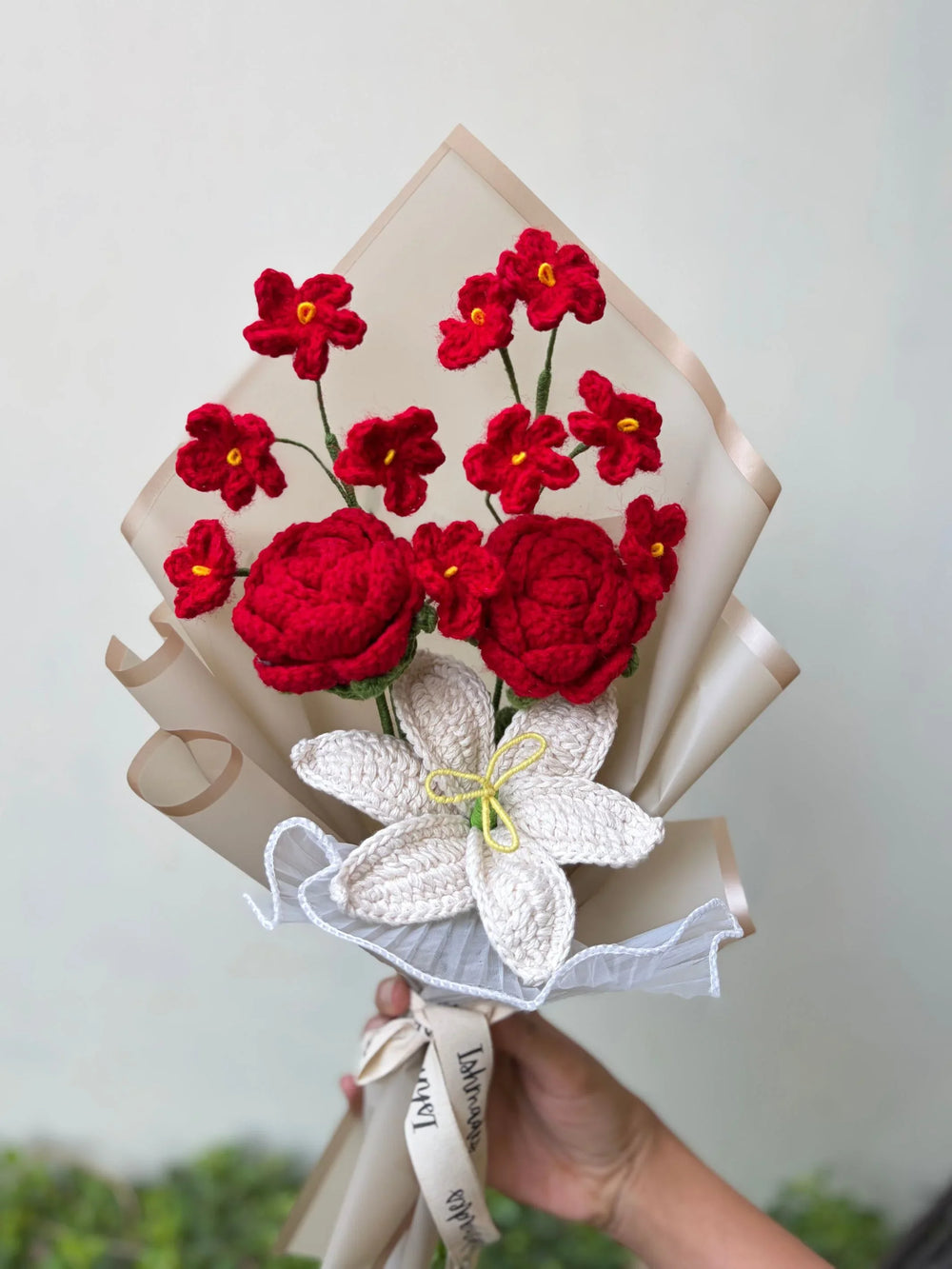 Hand holding a bouquet of red and white crochet flowers wrapped in beige paper