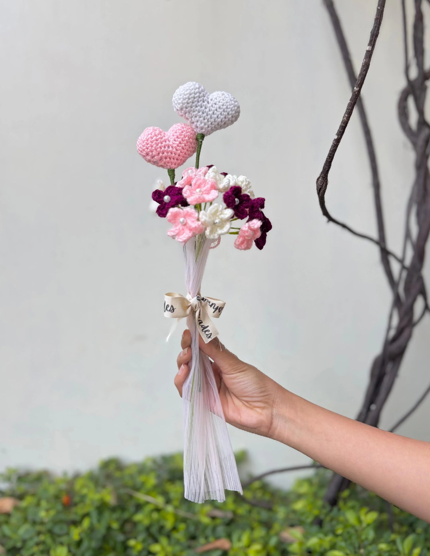 Hand holding crochet heart and flower bouquet with ribbon outdoors